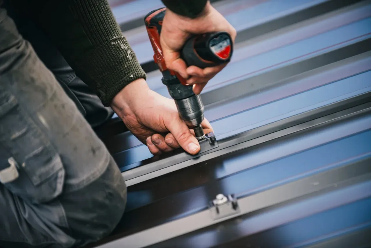 Builder fastening dark metal roof panels with a drill